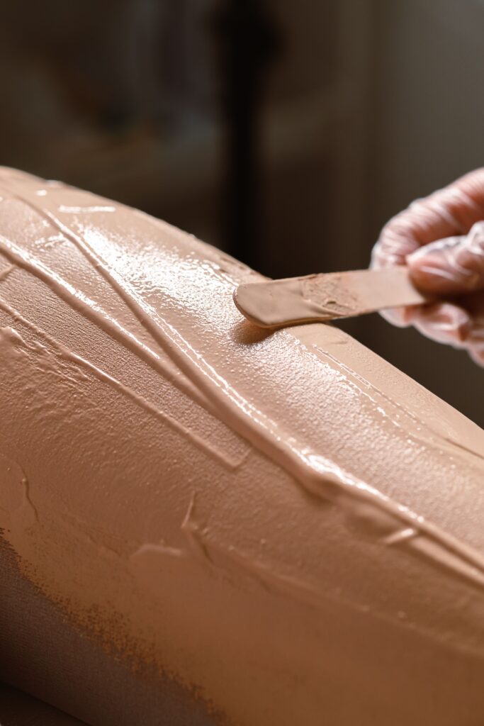 Detailed close-up of a hand applying skincare cream with a wooden stick on skin.